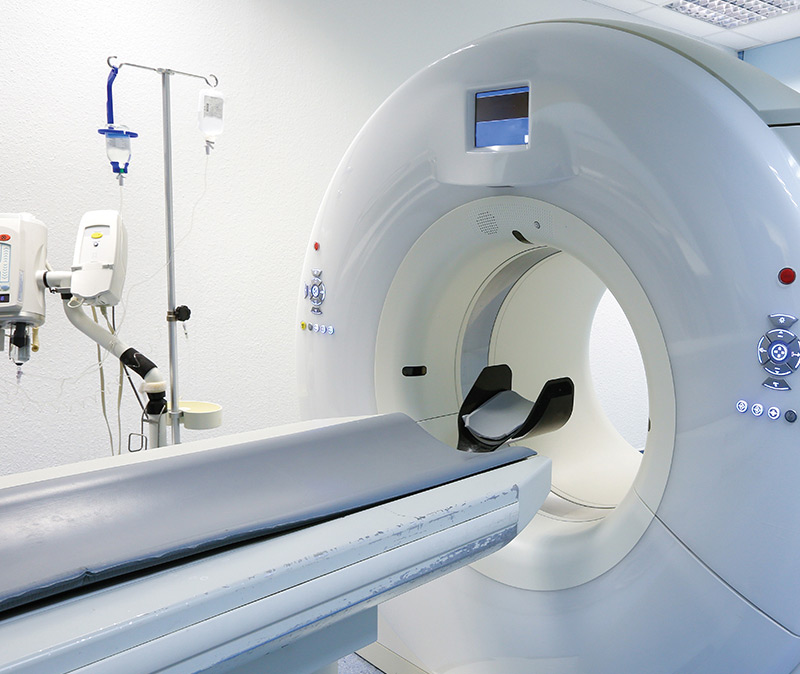 Imaging - A CT scanner in a medical imaging room, showing the patient table and circular scanning machine with control panels.